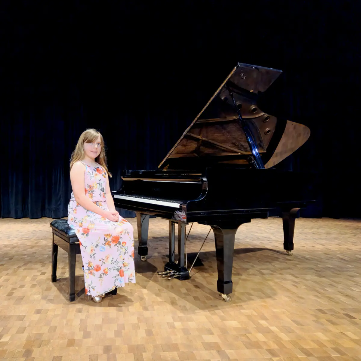 An OC Piano Program student seated beside the grand piano at the annual recital