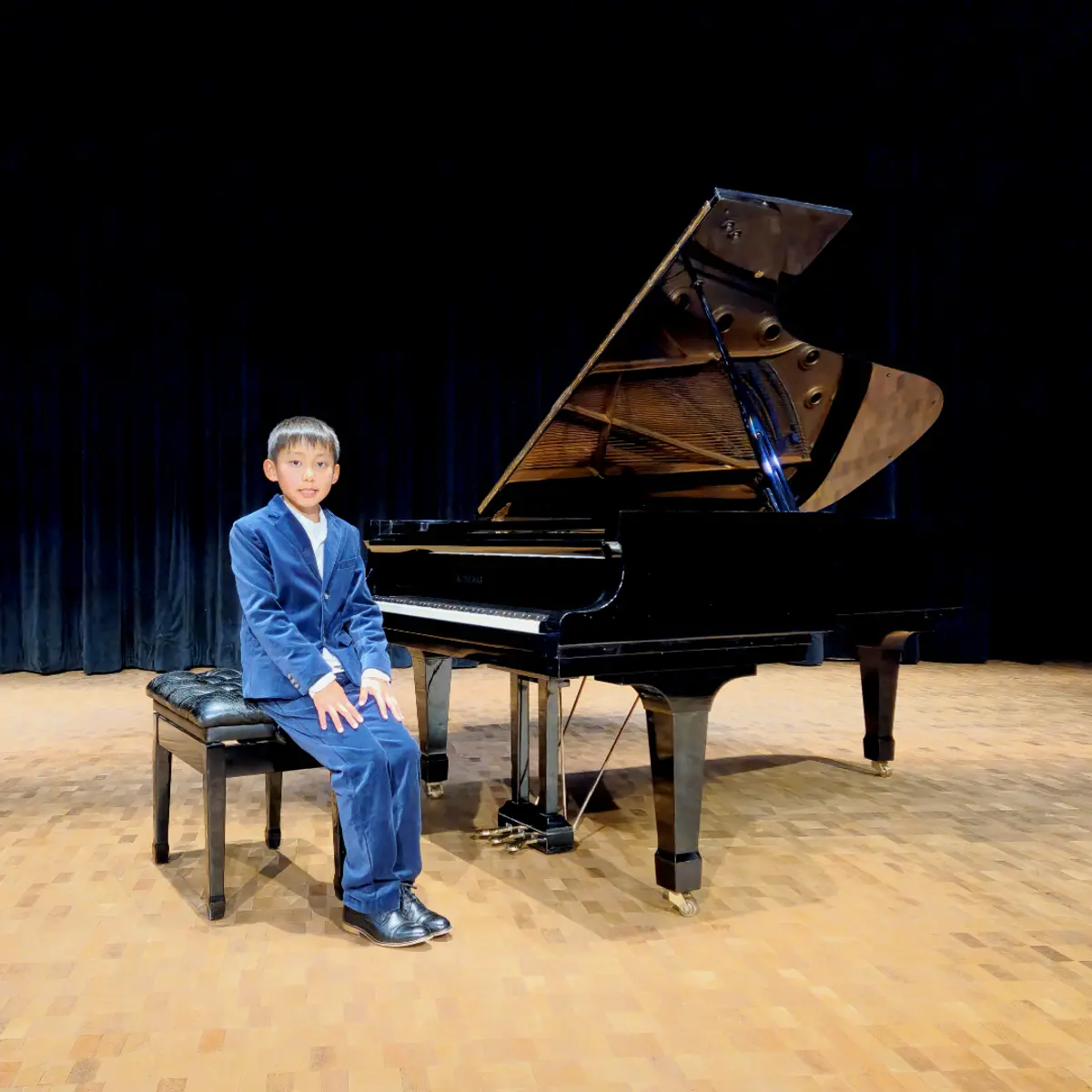 An OC Piano Program student seated beside the grand piano at the annual recital