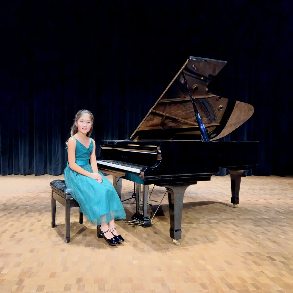 An OC Piano Program student seated beside the grand piano at the annual recital