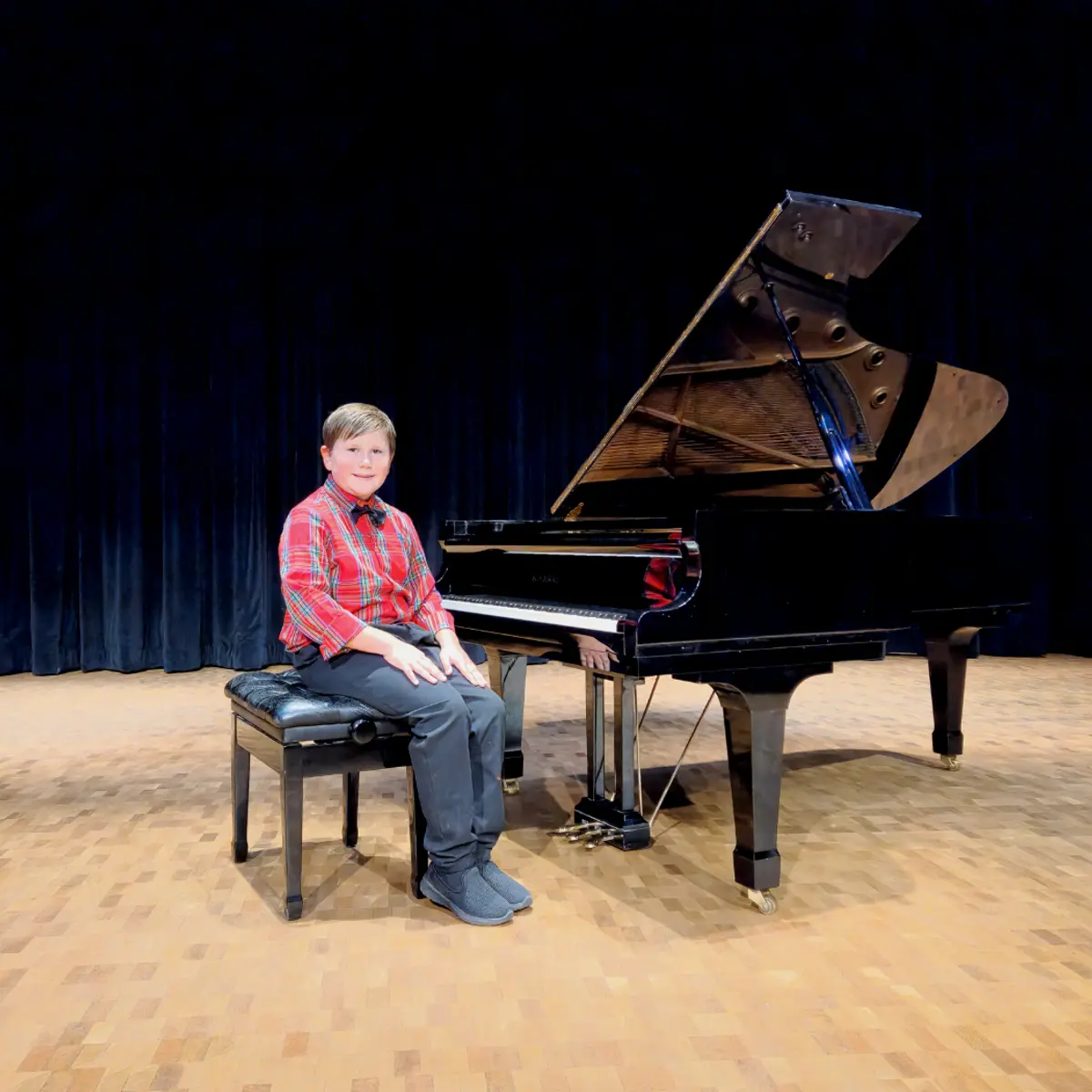 An OC Piano Program student seated beside the grand piano at the annual recital
