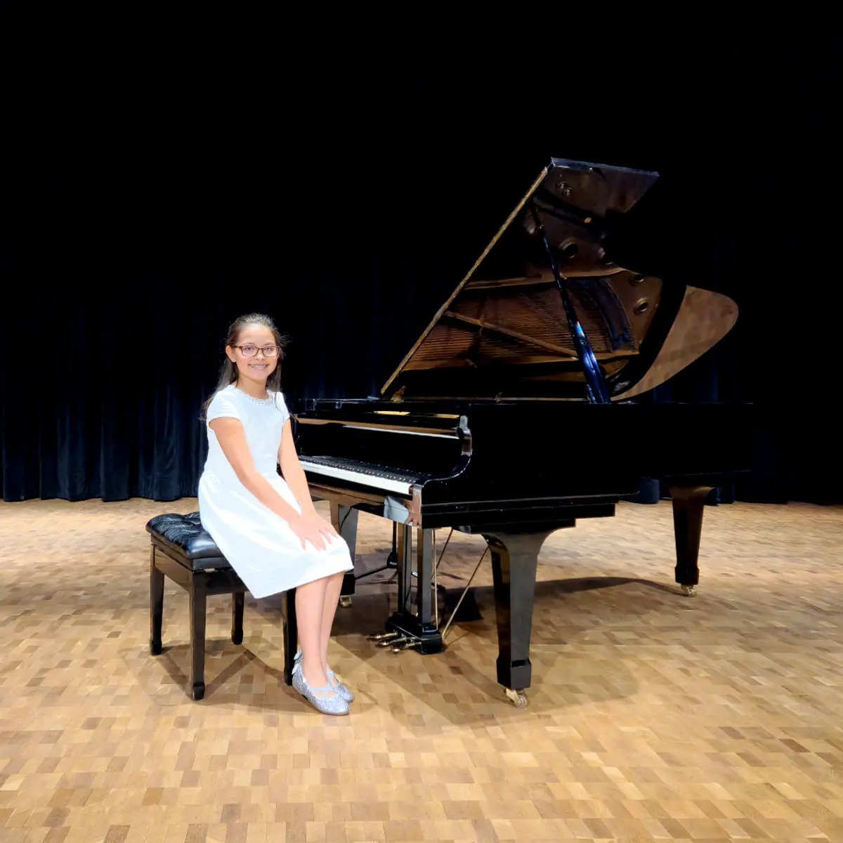 An OC Piano Program student seated beside the grand piano at the annual recital