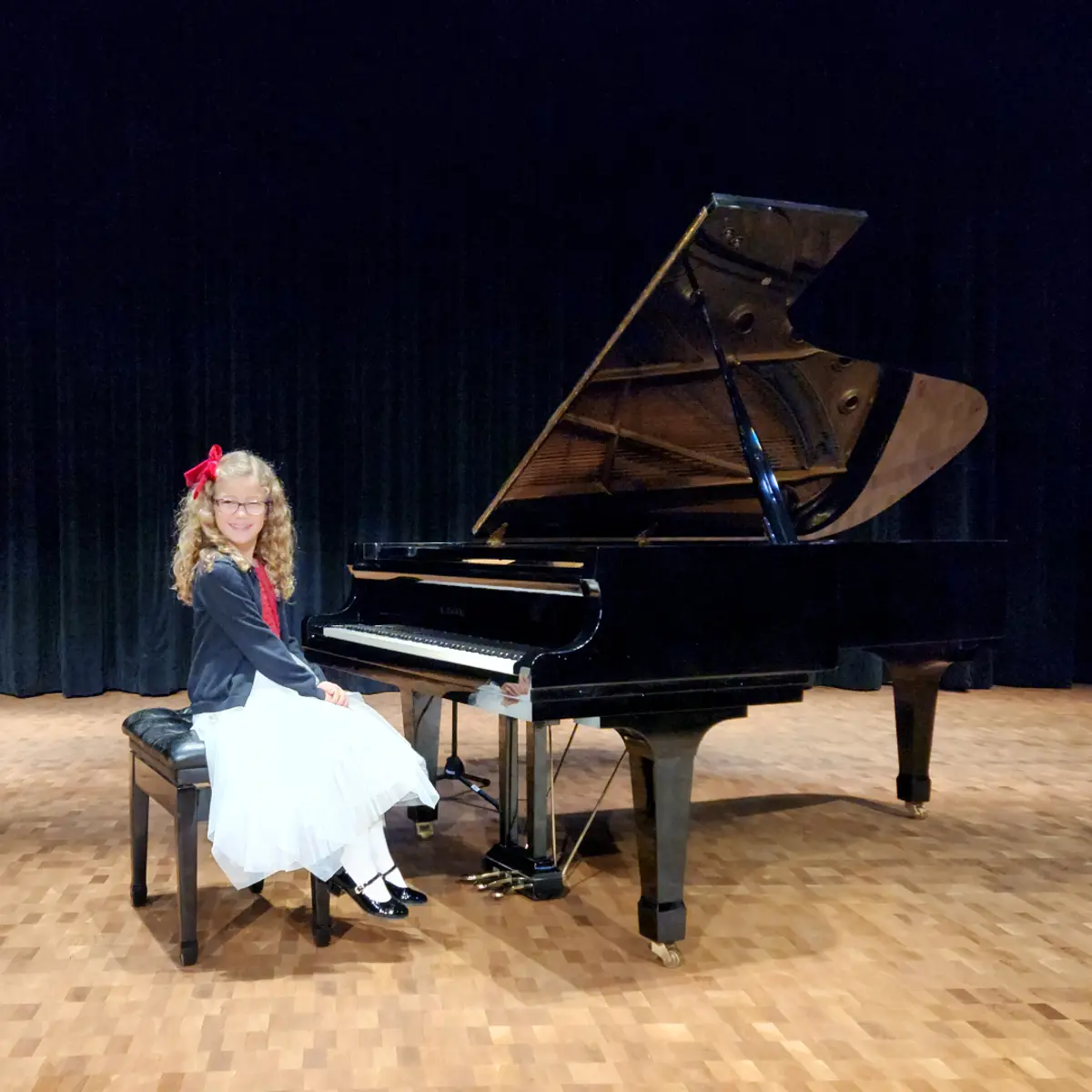 An OC Piano Program student seated beside the grand piano at the annual recital