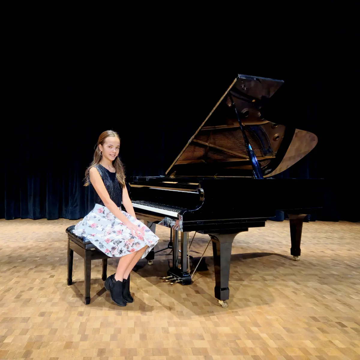 An OC Piano Program student seated beside the grand piano at the annual recital